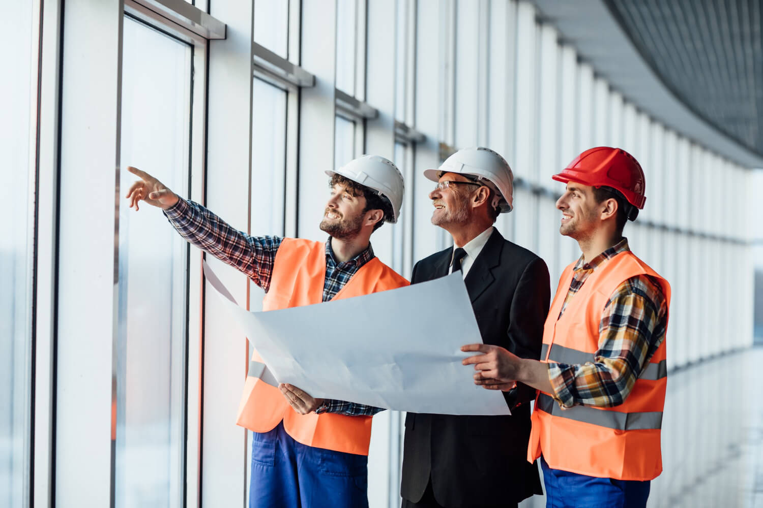 Three men in hard hats and safety vests looking out a window.